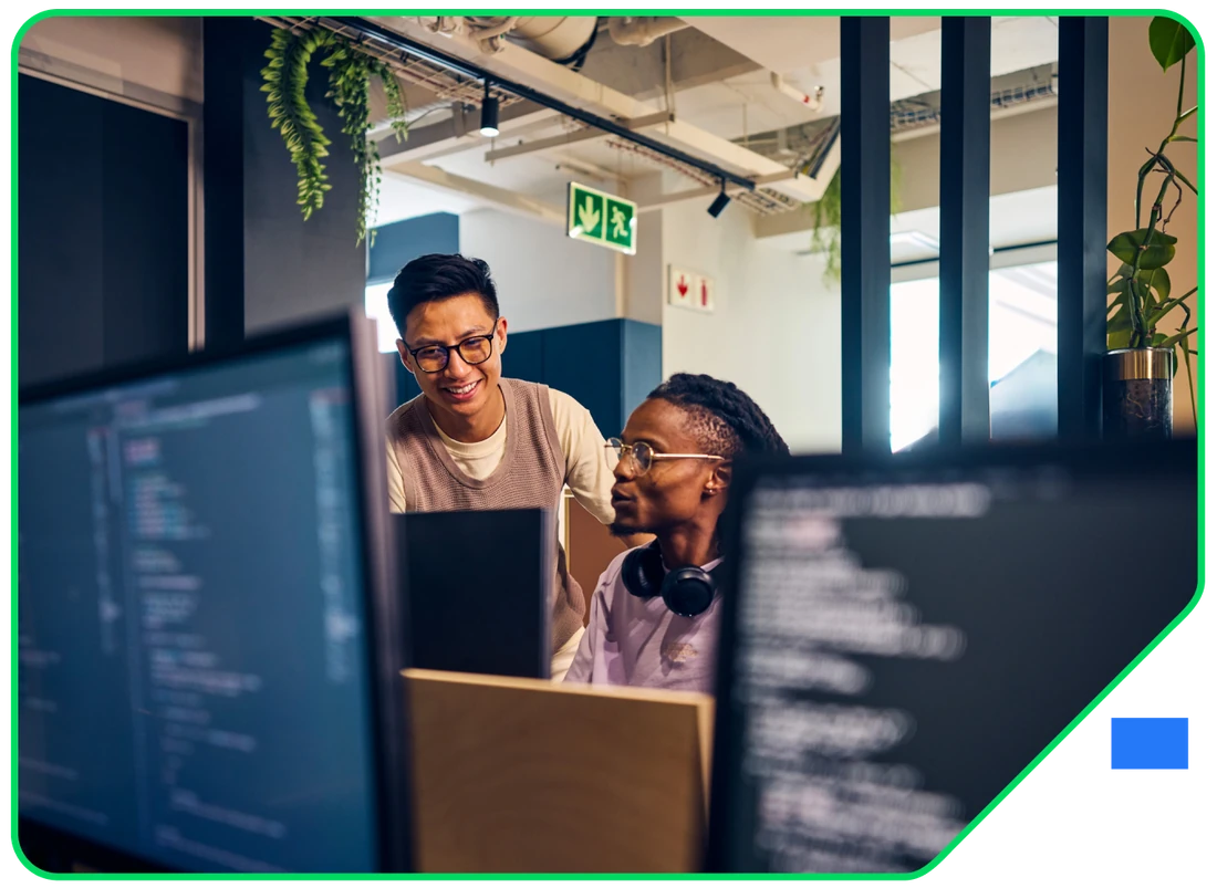Two developers reviewing code together between monitors in the studio