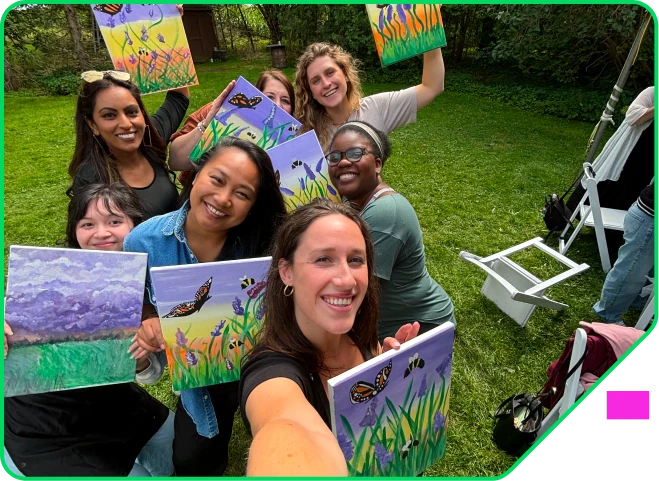 Colleagues holding up their finished canvases at an outdoor team paint night